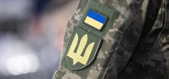Камуфляжний рукав військової форми з двома нашивками: прапор України синьо‑жовтий угорі та зелений щит із жовтим тризубом унизу