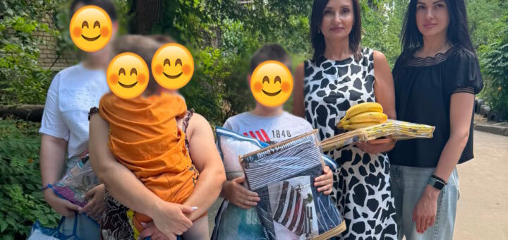 П’ятеро людей стоять на доріжці серед зелені, позаду — цегляна будівля. Чотири обличчя закриті смайликами. Двоє тримають великі подушки «Viluta Relax Collection», інші — дитину в помаранчевому одязі, банани та складені речі.