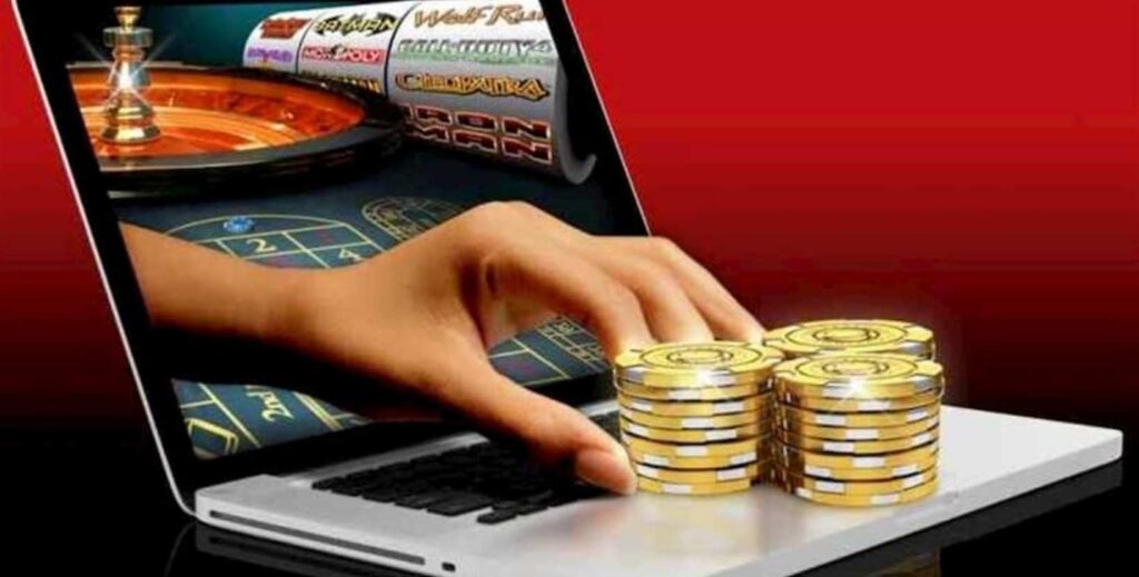 Інформаційна графіка: ноутбук із зображенням рулетки та слотів на екрані; з екрану виходить рука, яка тягнеться до золотих фішок на клавіатурі; фон червоно‑чорний, що підкреслює тему азартних ігор