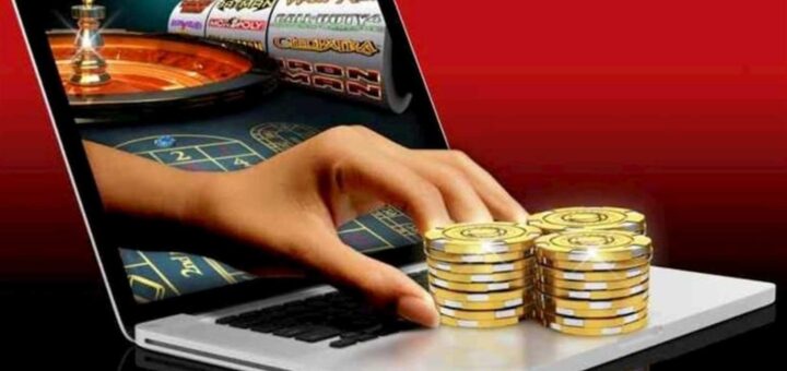 Інформаційна графіка: ноутбук із зображенням рулетки та слотів на екрані; з екрану виходить рука, яка тягнеться до золотих фішок на клавіатурі; фон червоно‑чорний, що підкреслює тему азартних ігор