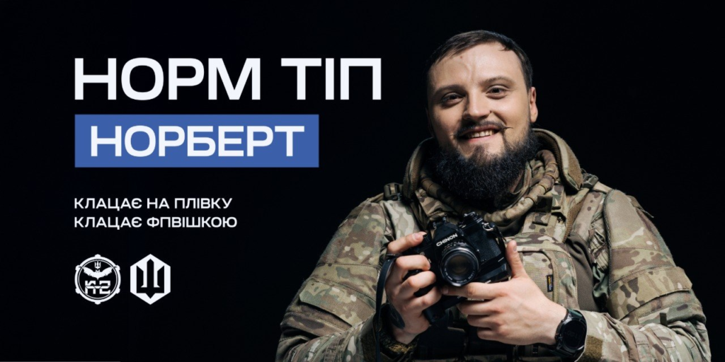 Інформаційний постер українською мовою: чоловік у камуфляжному одязі тримає фотокамеру Chinon; темний фон; ліворуч текст — “Норм тіп Норберт. Клацає на плівку. Клацає FPVшкою”; унизу два логотипи — круглий зі стилізованими елементами та інший у формі тризуба.