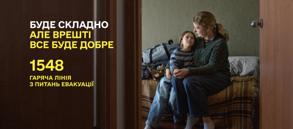 Інформаційний постер українською мовою: у кімнаті на ліжку сидять дорослий і дитина, поруч сумки та м’яка іграшка; дорослий обіймає дитину; ліворуч білий і жовтий текст — “Буде складно, але врешті все буде добре. 1548 Гаряча лінія з питань евакуації”.