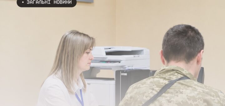 Інформаційне фото: двоє людей сидять за столом у кабінеті; один у білій сорочці з синім бейджем, інший — у камуфляжній формі; позаду видно принтер; текст — “ЗАГАЛЬНІ НОВИНИ”.