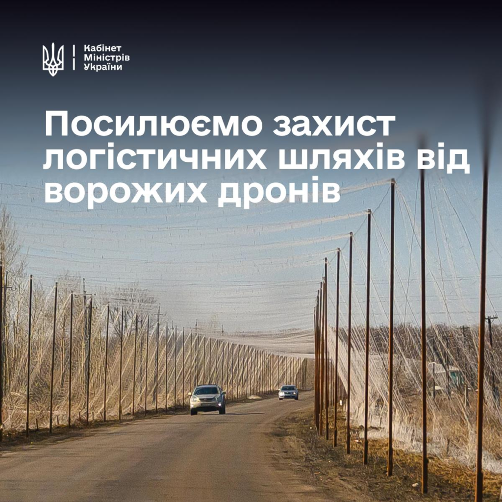 Інформаційний постер українською мовою: сільська дорога з автомобілями, над дорогою встановлені металеві конструкції з сітками для захисту від дронів; обабіч — суха трава та дерева без листя; угорі — емблема Кабінету Міністрів України; текст — “Посилюємо захист логістичних шляхів від ворожих дронів”.