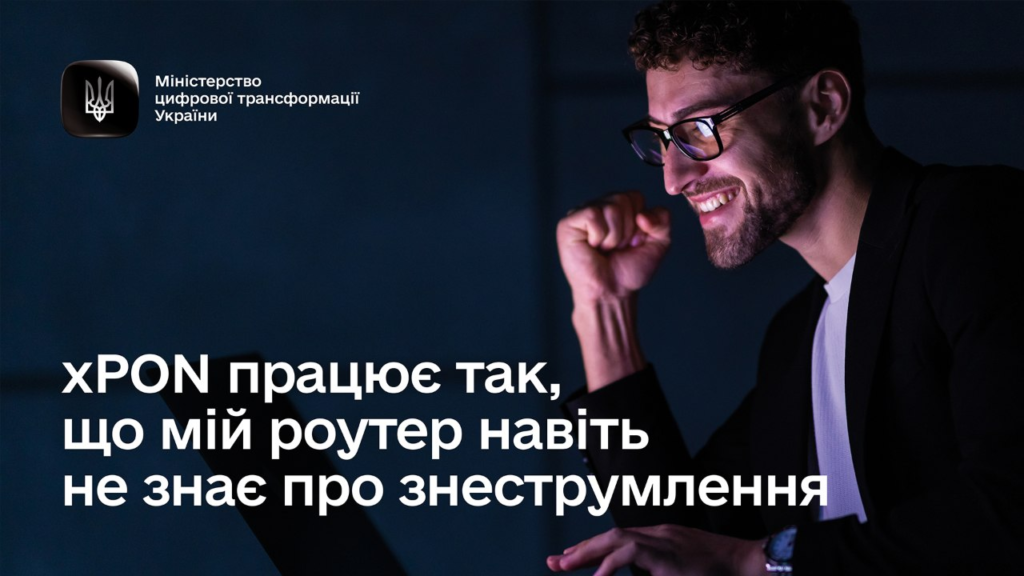 Людина в окулярах і темній куртці сидить перед комп’ютером, піднявши кулак у жесті задоволення. Угорі ліворуч логотип Міністерства цифрової трансформації України.
