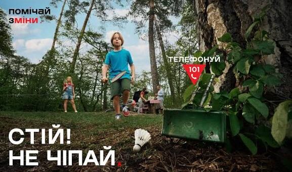 Дитина у парку помічає зелений металевий ящик біля дерева, поруч лежить волан для бадмінтону; на плакаті написано українською: «Помічай зміни», «Телефонуй 101», «Стій! Не чіпай».