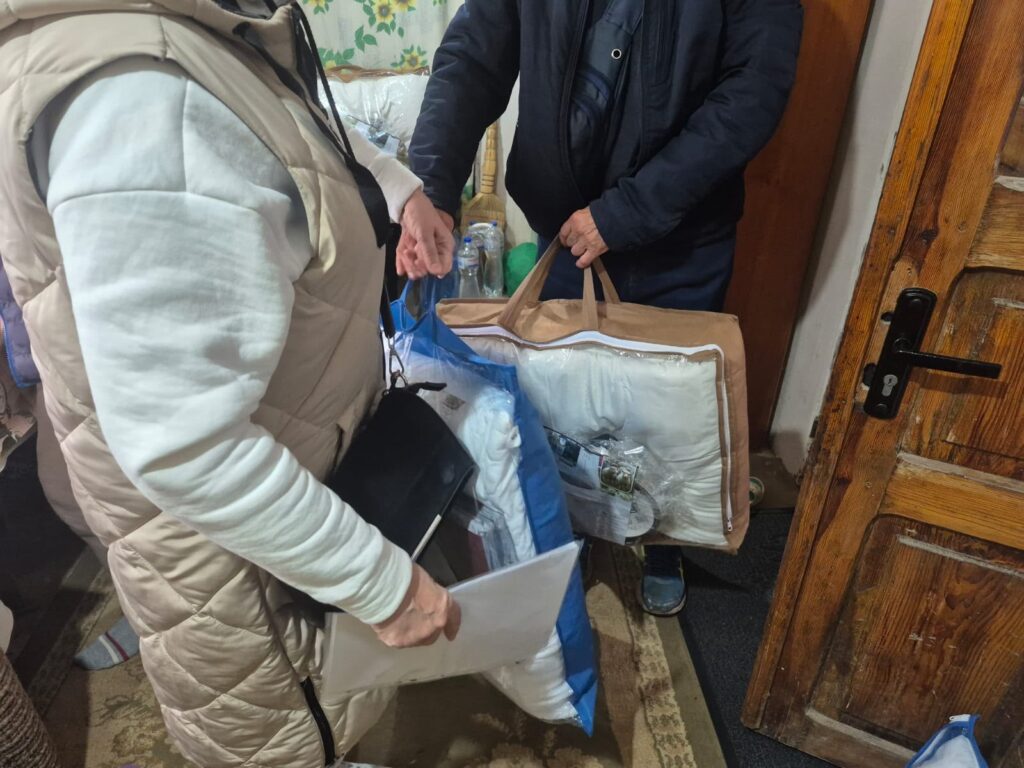 Передача гуманітарної допомоги біля приватного будинку: люди тримають подушки, ковдри та пакунок із речами.